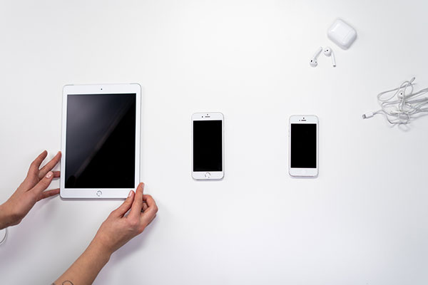 Tablet, two smartphones, and wireless and wired earbuds on a white surface