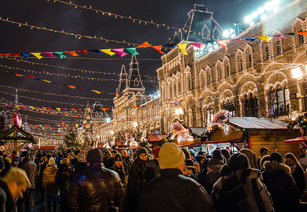 Crowds browse outdoor market stalls beneath strings of lights beside an illuminated building.