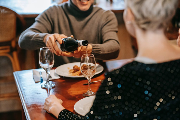 A diner pours wine for another person across a restaurant table.