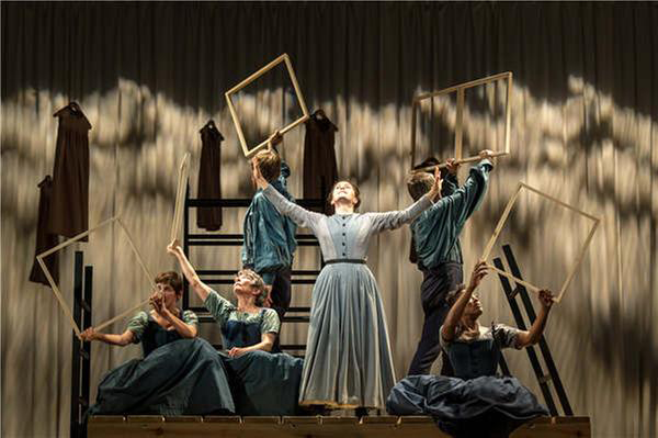 Stage performers holding empty frames around a woman with outstretched arms