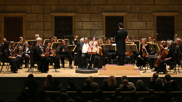 An orchestra performs onstage with a conductor and seated audience.