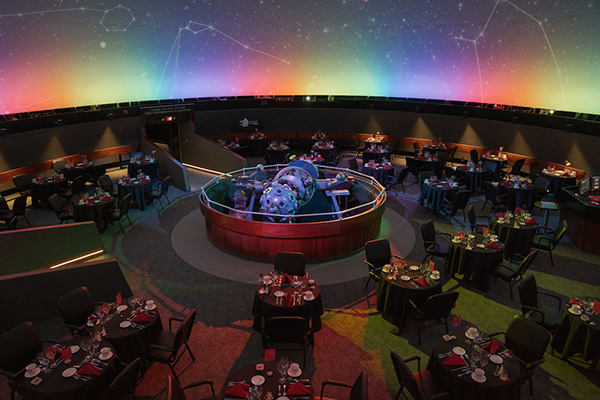 Banquet tables arranged around a planetarium projector beneath colorful constellation projections