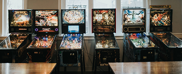 A row of six pinball machines with colorful backboards.