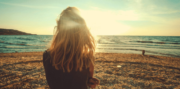 A person stands alone on a beach, facing the ocean in golden sunlight.