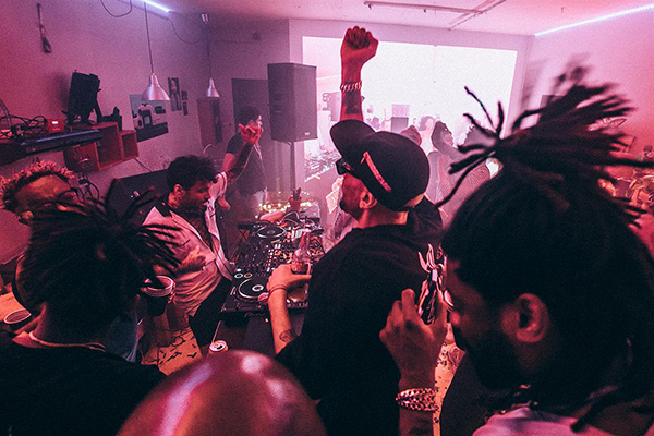 Partygoers dancing around DJ equipment in a pink-lit room.