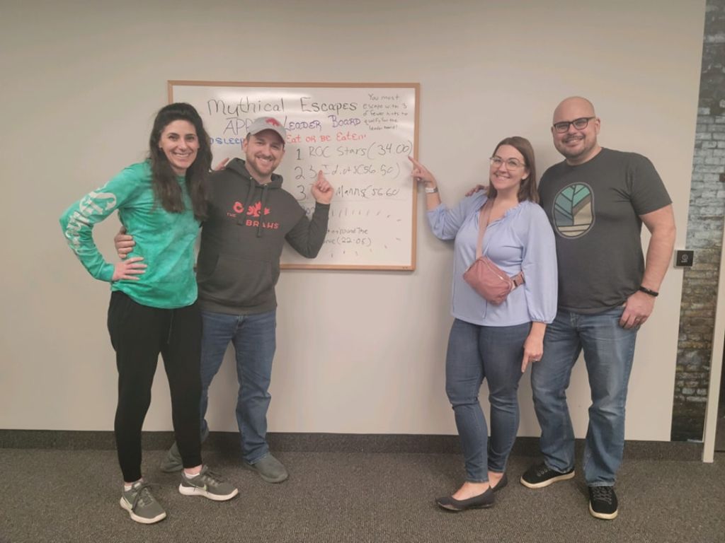 Four adults posing beside a leaderboard.