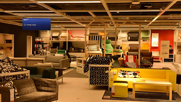 A furniture showroom displays sofas, armchairs, tables, and shelving, including a bright yellow sofa.