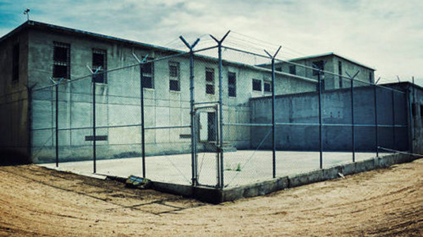 Prison-style building and yard enclosed by tall chain-link fencing
