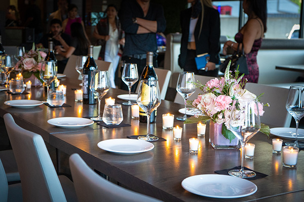 A long dining table is set with plates, wine glasses, candles, and pink and white flowers.