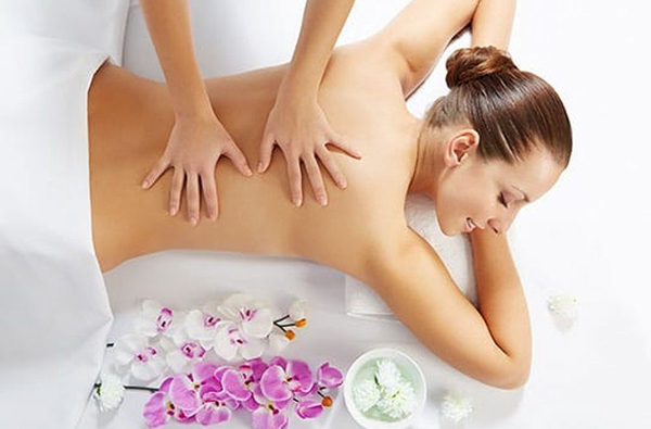 A massage therapist massages a woman lying face down on a treatment table.