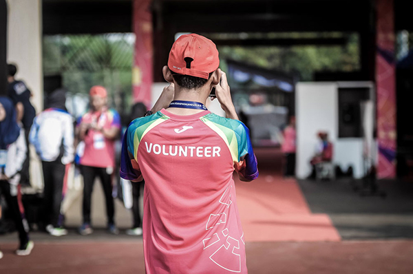 A person in a red cap wears a brightly colored shirt marked “VOLUNTEER.”