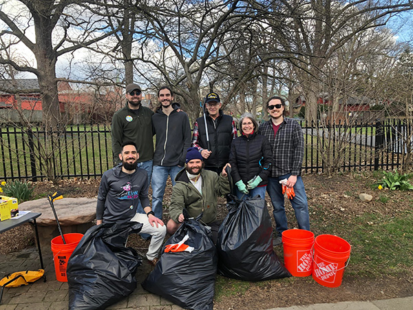 A group posing outdoors with filled trash bags, gloves and cleanup buckets.