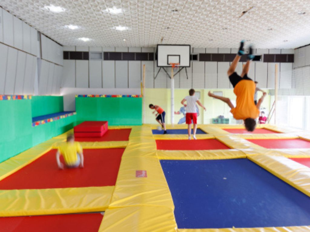 People jump on padded indoor trampolines while one person flips upside down.
