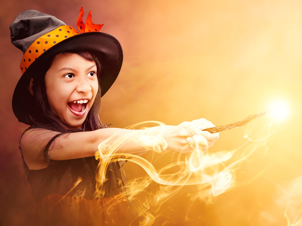 Child in a witch hat pointing a wand surrounded by glowing magical effects.
