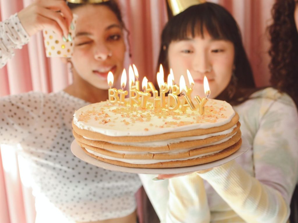 Partygoers celebrate with a sprinkle-covered cake topped with lit “HAPPY BIRTHDAY” candles.