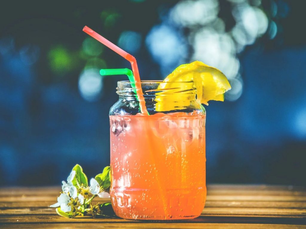 Pink-orange iced drink in a jar with a lemon slice and colorful straws