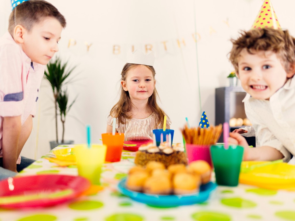 Children in party hats gathered around a table with cake, snacks and colorful cups