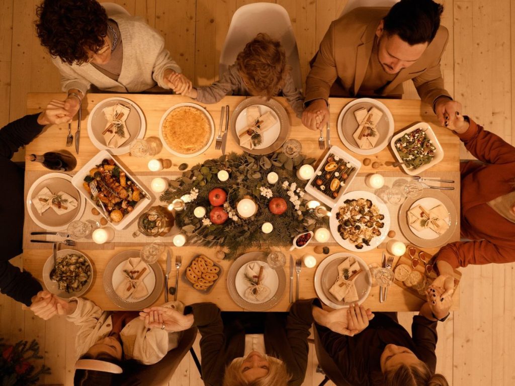 Guests holding hands around a candlelit dinner table set with shared dishes.
