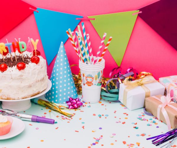 Birthday table with a cherry-topped cake, wrapped gifts, party hats and colorful bunting