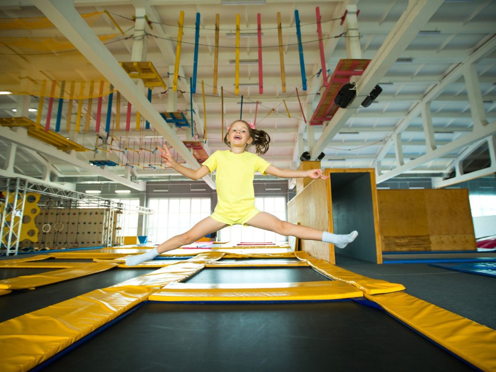 Child jumping with legs outstretched at an indoor trampoline park.