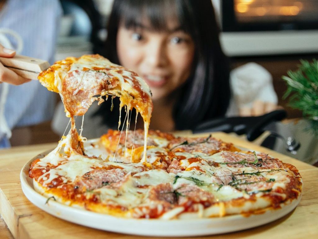 Slice of pizza being lifted with melted cheese stretching from the plate