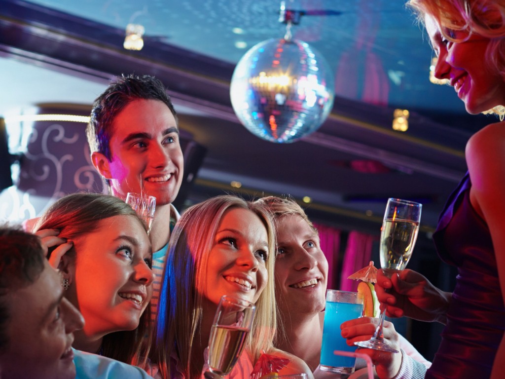 A smiling group holds champagne flutes and a blue cocktail beneath a disco ball.