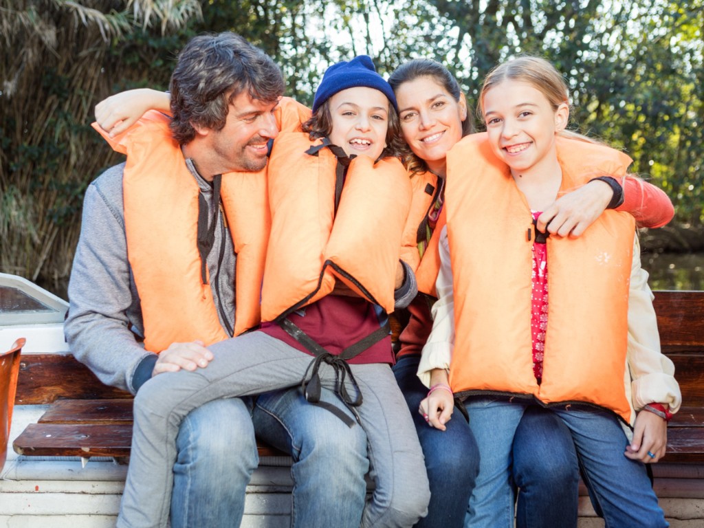 Two adults and two children wearing orange life jackets sit together on a boat.