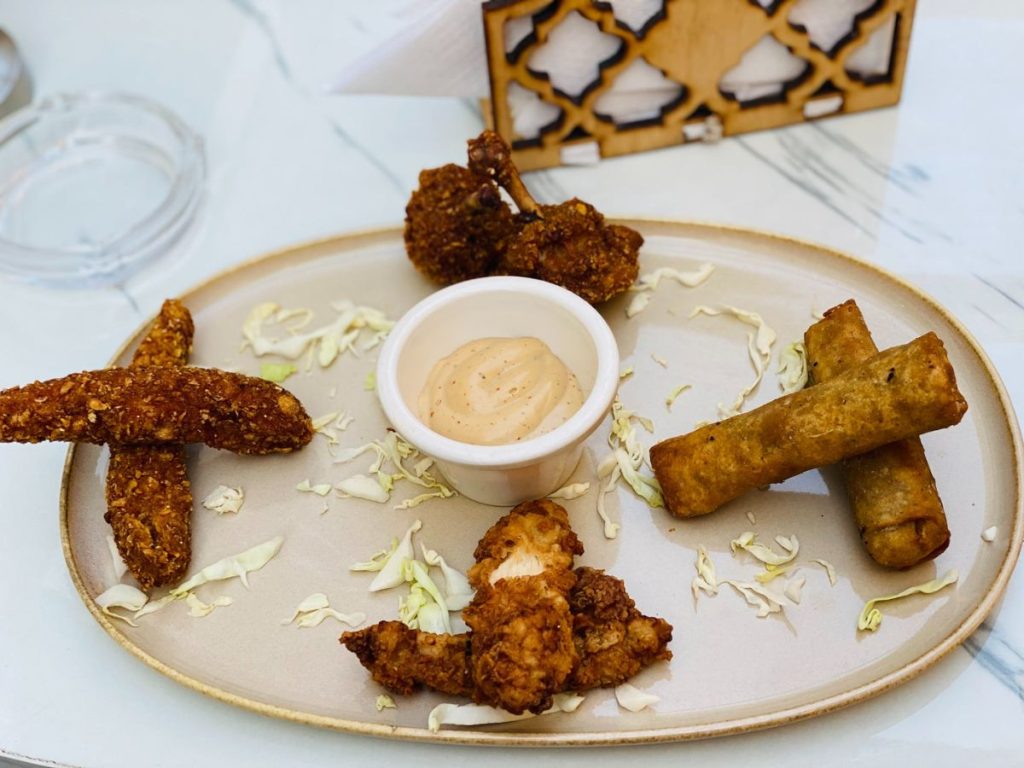 Platter of fried finger foods and spring rolls surrounding a bowl of dipping sauce.