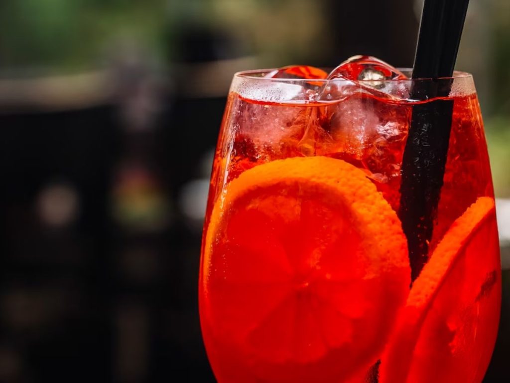 Red-orange iced drink with orange slices and black straws