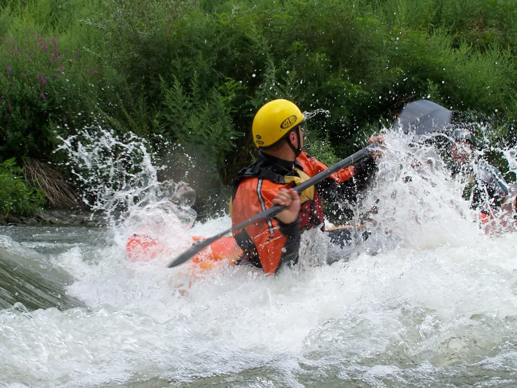 Helmeted kayaker paddling an orange kayak through whitewater