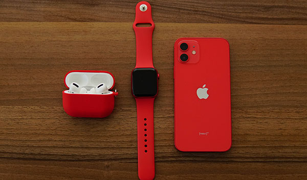 Red Apple Watch and iPhone beside AirPods in a red charging case