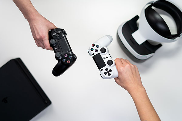 Two people holding PlayStation controllers beside a console and VR headset