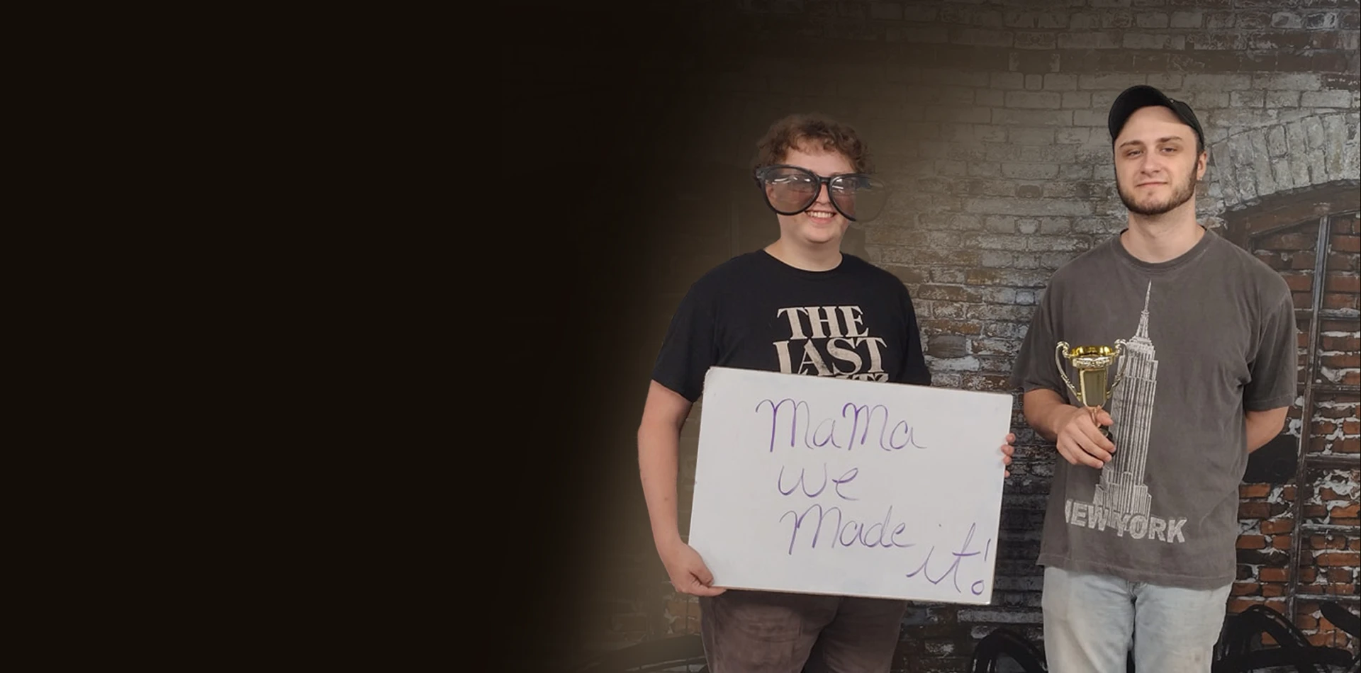 Two players hold a handwritten sign in front of a game-room backdrop.