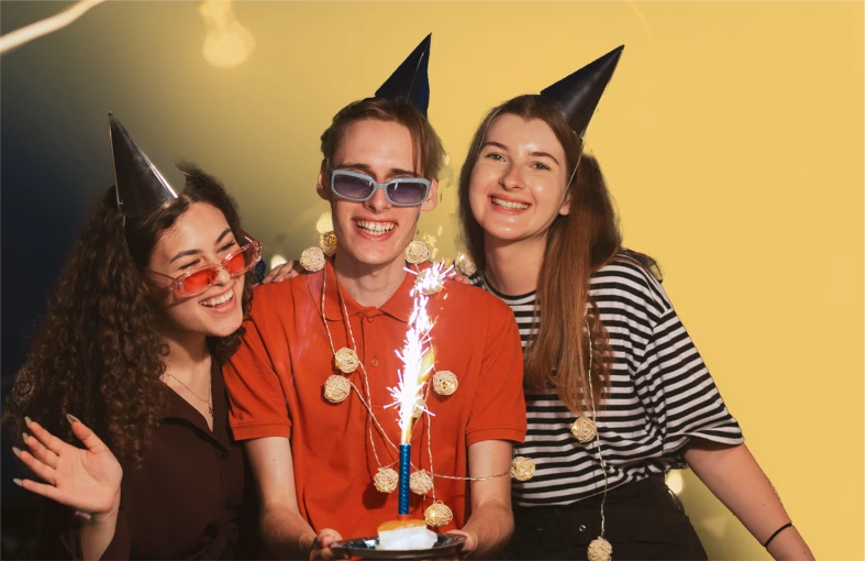 Friends in party hats celebrate around a cake with a sparkling candle.