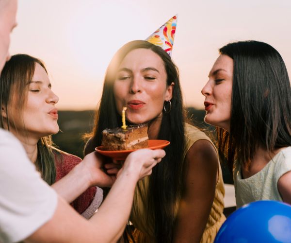 Three women celebrating a birthday with cake and candle at party