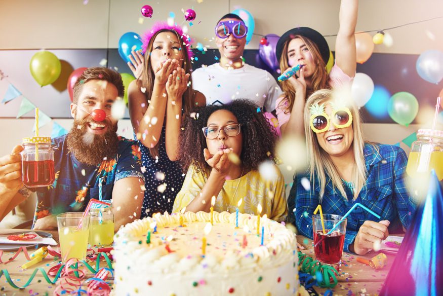 Group of friends celebrating with birthday cake, balloons, and confetti
