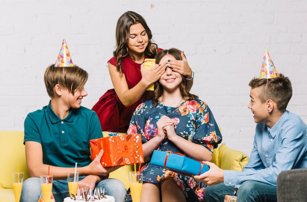 Teens at birthday party with gifts and cake wearing colorful party hats
