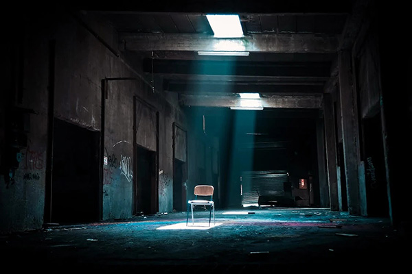 A single chair in a dark, derelict concrete room lit by overhead windows