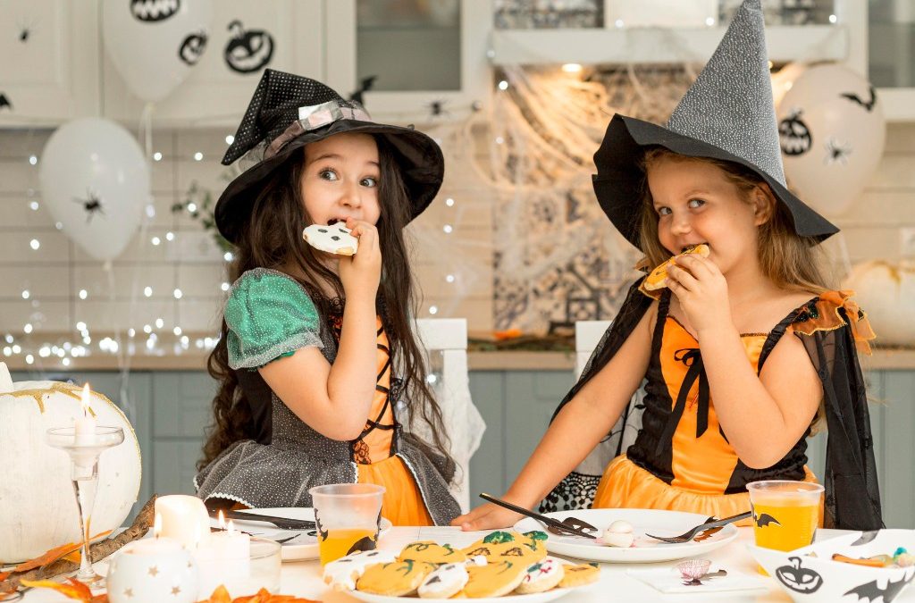 Two girls in witch costumes eating Halloween cookies at decorated party table