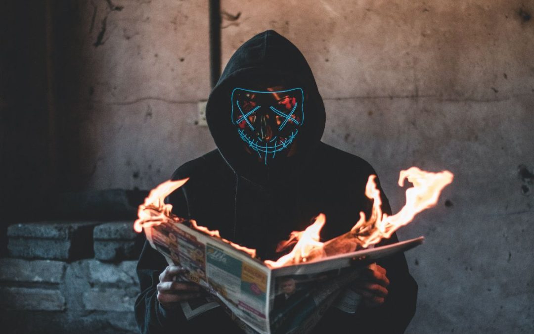 Person in hooded sweatshirt wearing illuminated neon mask holding flaming book