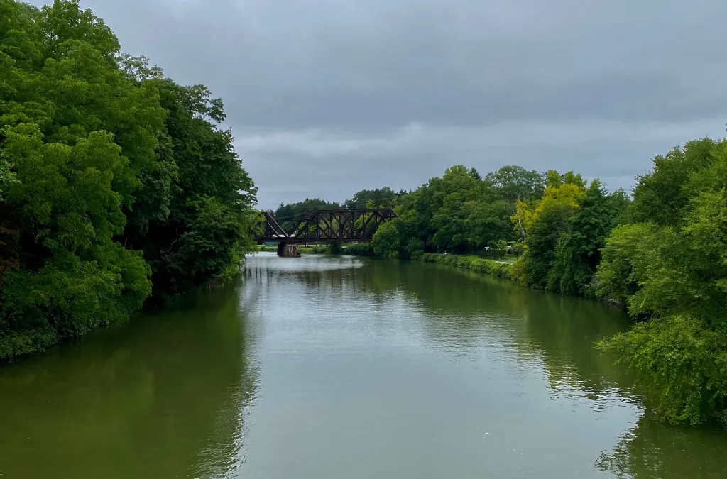 Calm river lined with green trees and railroad bridge in Pittsford