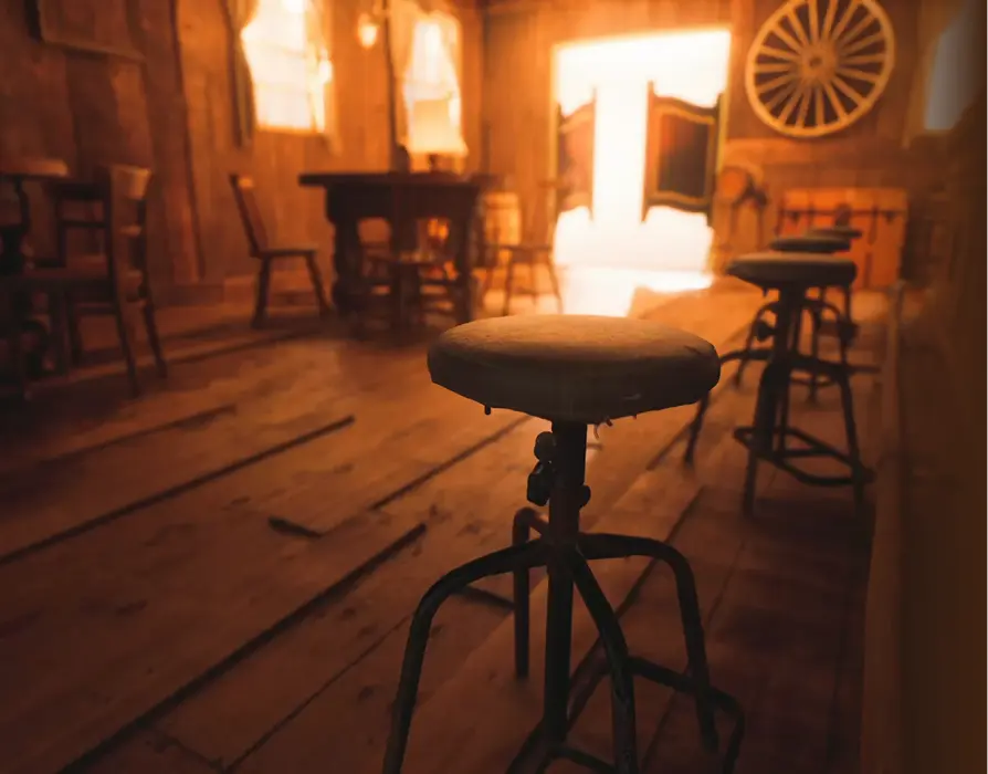 The wood-paneled Saloon room with a round table and bar stools.